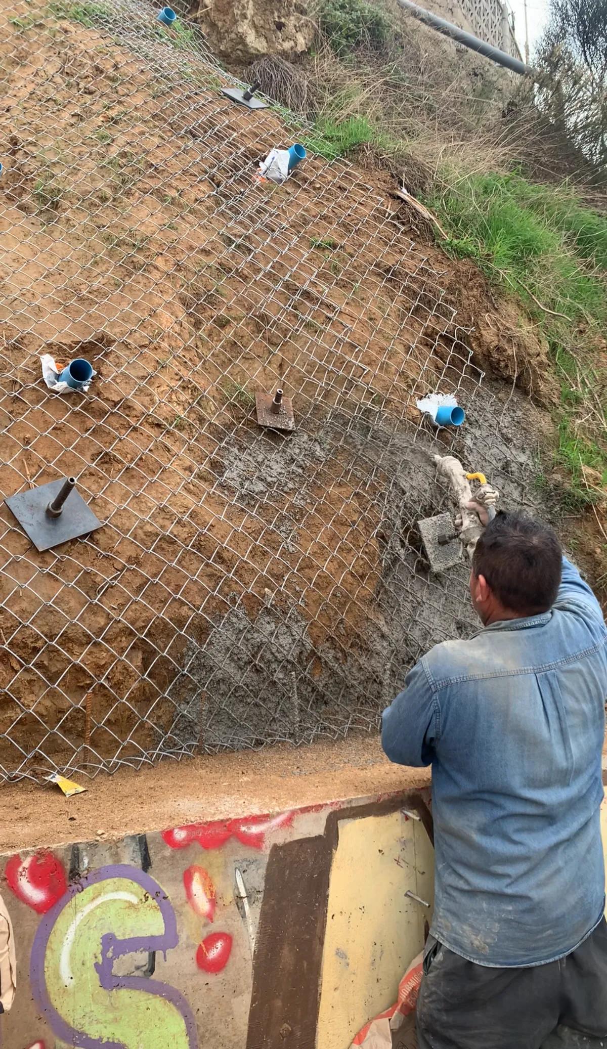 Operador iniciando la proyección neumática de shotcrete en un talud de tierra