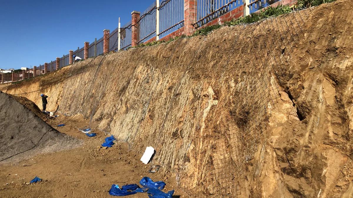 Trabajadores instalando una gran malla de acero de fortificación sobre la superficie inclinada de un talud